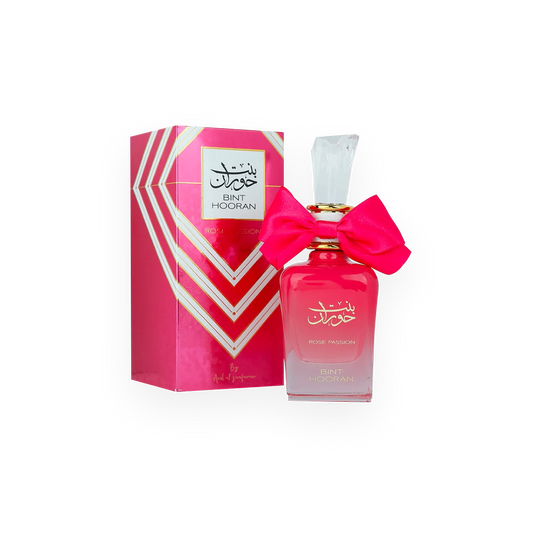 Une bouteille de parfum rose vif appelée "Bint Hooran Rose Passion" de la marque Ard Al Zaafaran, présentée dans un flacon élégant avec un grand nœud rose attaché autour du col et un bouchon transparent. La boîte d'emballage, assortie à la couleur du flacon, affiche des motifs géométriques avec des accents dorés et le nom du produit en arabe et en anglais.