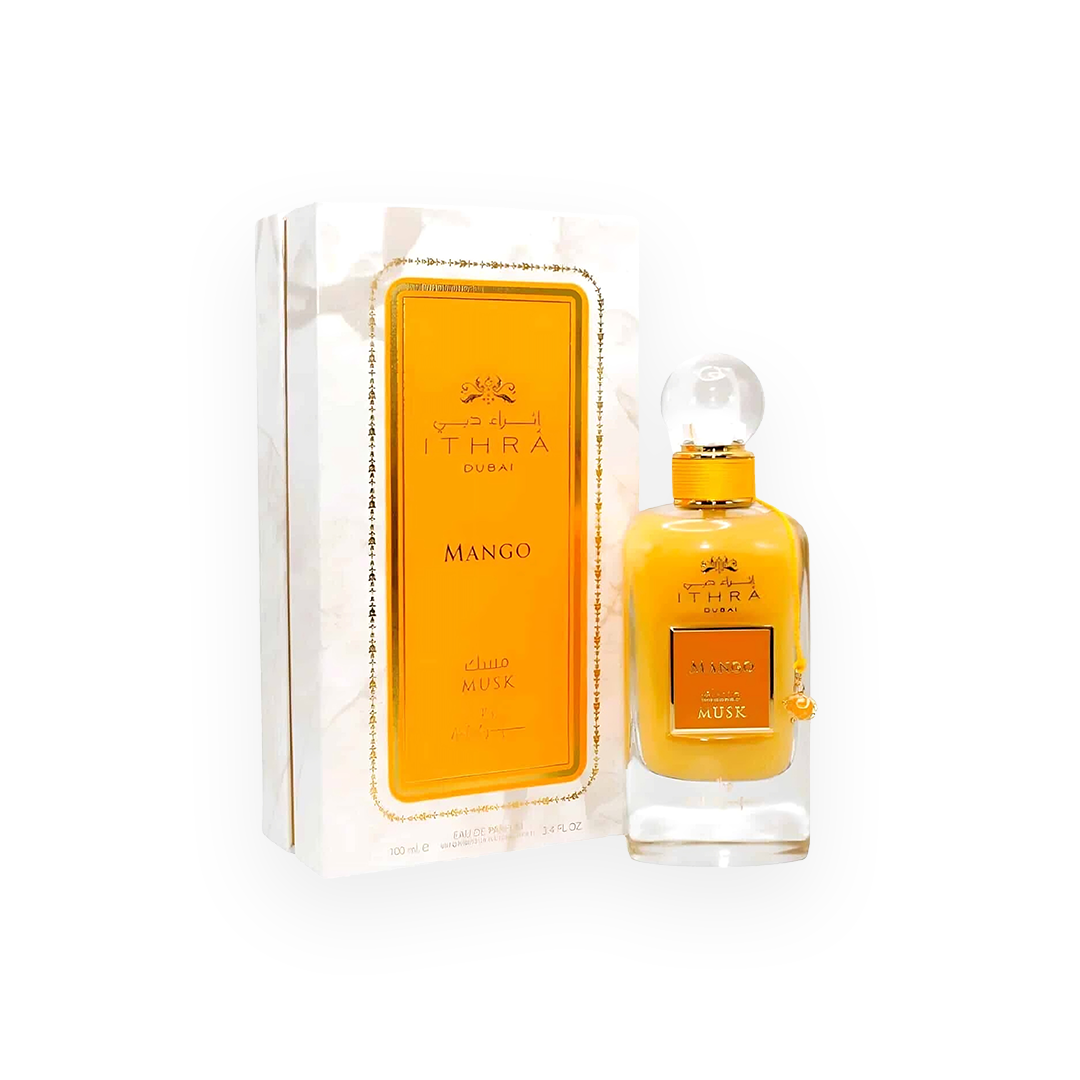 n flacon de parfum orange vif appelé "Mango Musk" de la marque Ithra Dubai par Ard Al Zaafaran. Le flacon sophistiqué est orné d'un bouchon sphérique transparent et d’un cordon assorti avec un pendentif doré. L'emballage présente un design élégant avec un fond marbré blanc, encadré d’accents dorés et une étiquette orange vibrant au centre, mettant en avant le nom du parfum en arabe et en anglais.