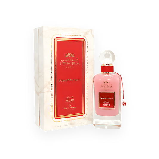 Un flacon de parfum rose doux appelé "Pomegranate Musk" de la marque Ithra Dubai par Ard Al Zaafaran. Le flacon élégant est surmonté d’un bouchon sphérique transparent et orné d’un cordon rouge avec un pendentif assorti. L’emballage présente un design luxueux avec un fond marbré blanc, des accents dorés et une étiquette rouge vibrante au centre, affichant le nom du parfum en arabe et en anglais.